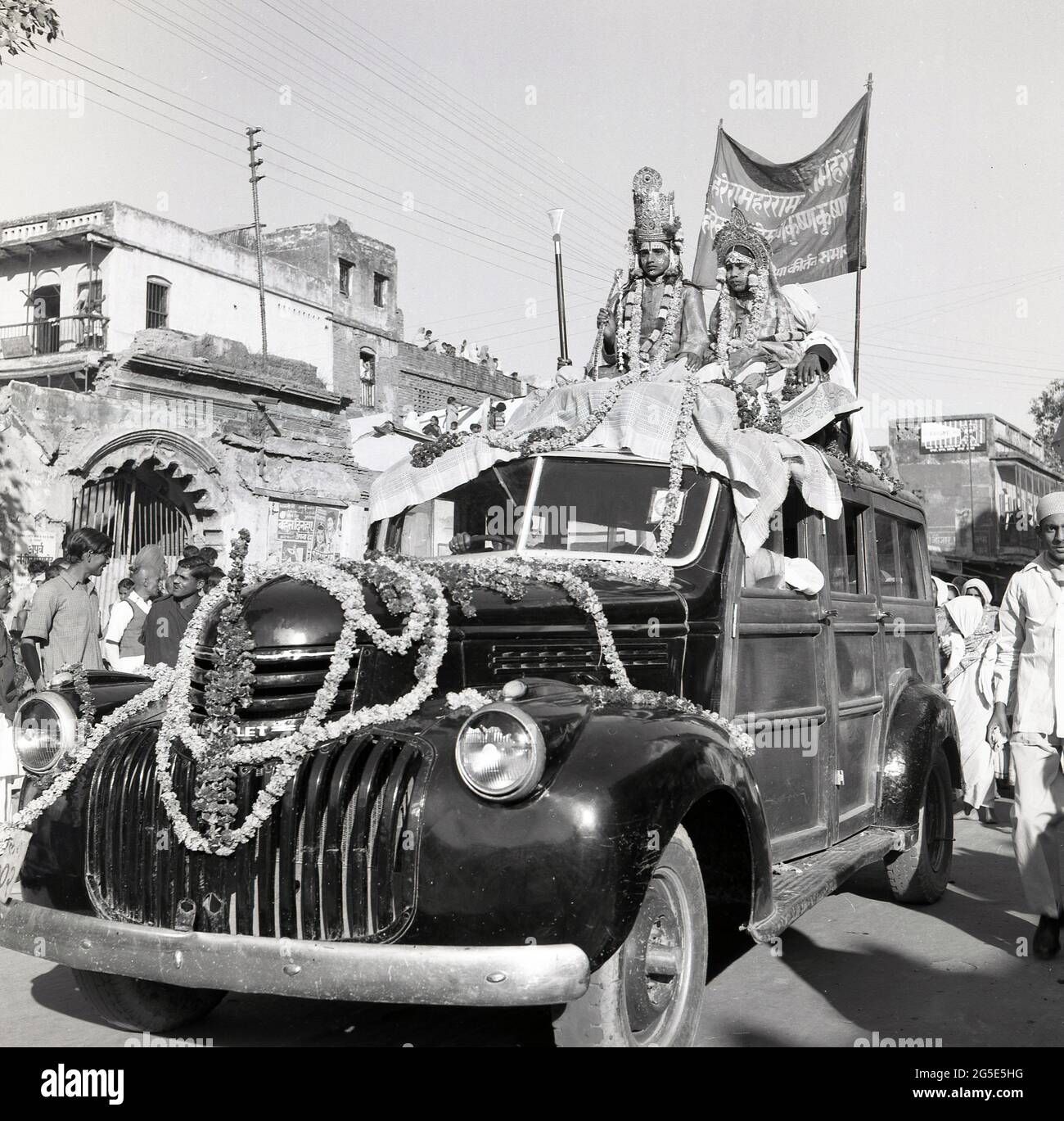 1950s, historical, wedding celebration, Benares, India, a newly married couple sitting on the roof of a wooden-framed Chevrolet van with the bonnet covered with decorated flower garlands or braids. Stock Photo