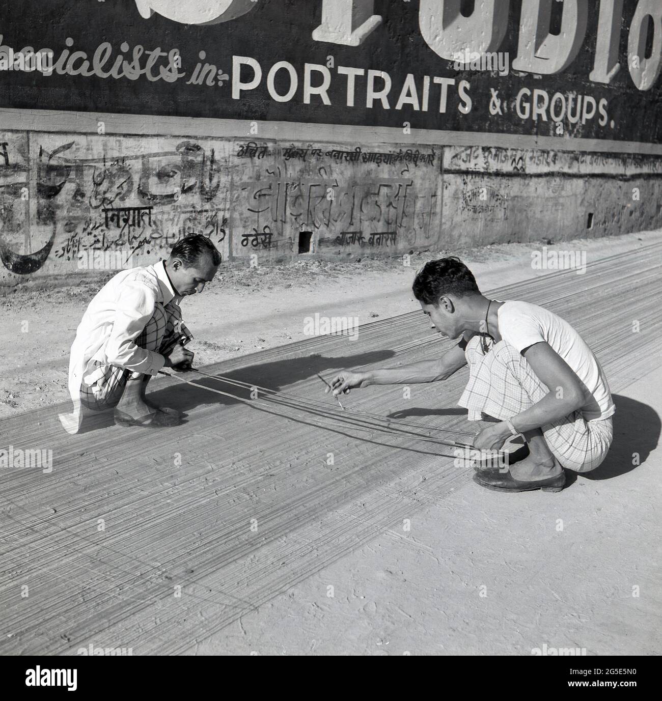 1950s, historical, outside in the street, two men stting on the dusty ground weaving, Benares, India. Stock Photo