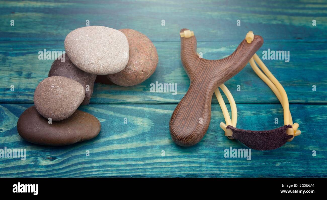 Slingshot and Five Smooth Stones on a Blue Table Stock Photo