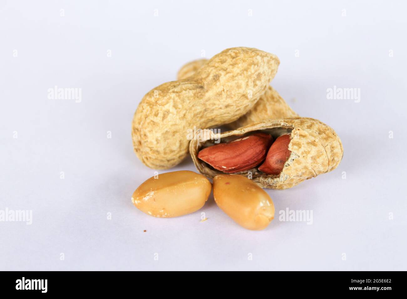 Peanuts isolated on white background . Two kernels are already unpacked. One of the peanuts, which was removed, revealed a red seed on the side. Stock Photo