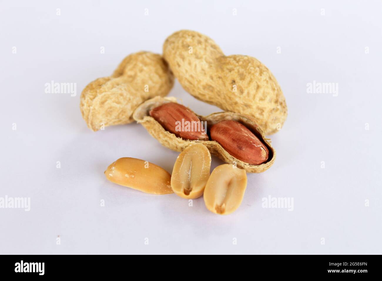 Peanuts isolated on white background . Two kernels are already unpacked. One of the peanuts unpacked reveals a red seed on the side. The seeds are sep Stock Photo