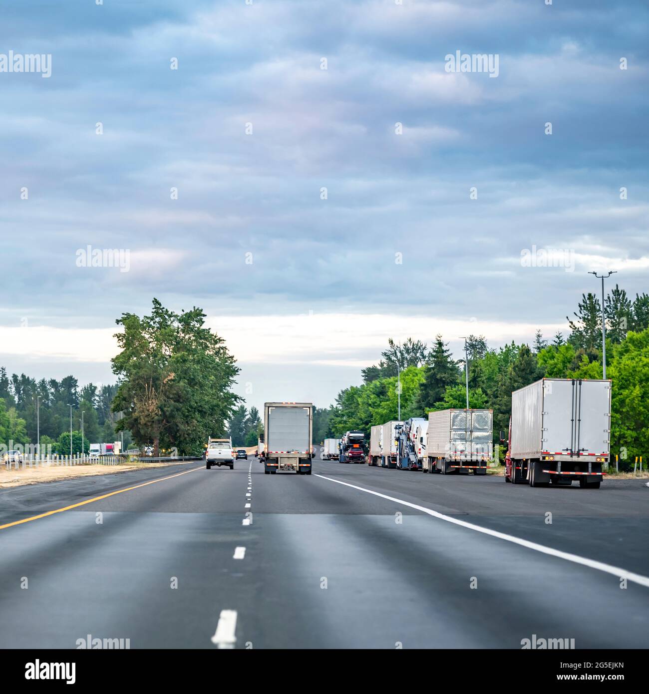Group of big rigs semi trucks tractors transporting cargo in different semi trailers standing in a line by the side of the highway road for a break ou Stock Photo
