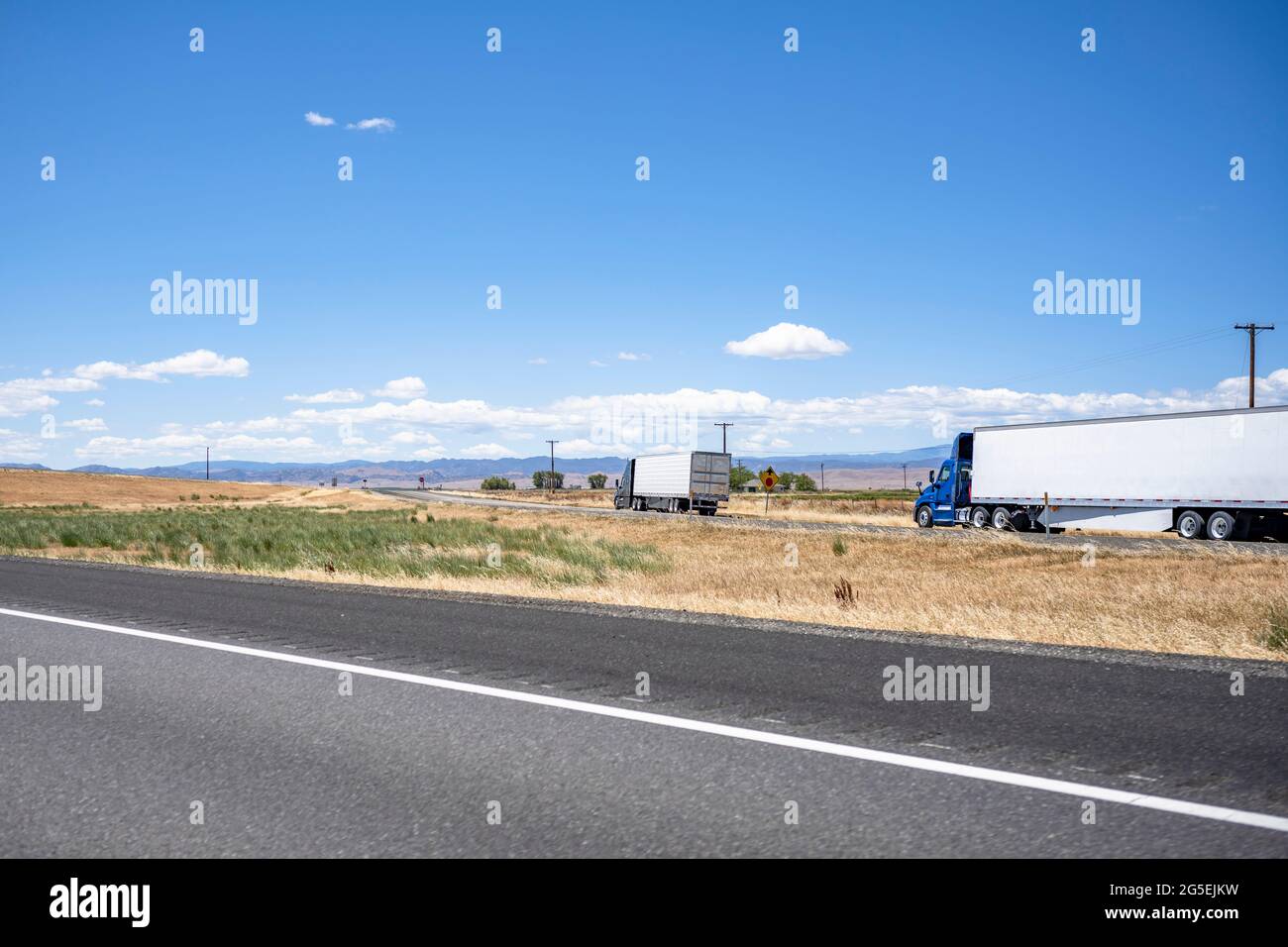 Group of big rigs semi trucks tractors caring cargo in different semi trailers standing on the shoulder of the highway exit intersection road take a b Stock Photo