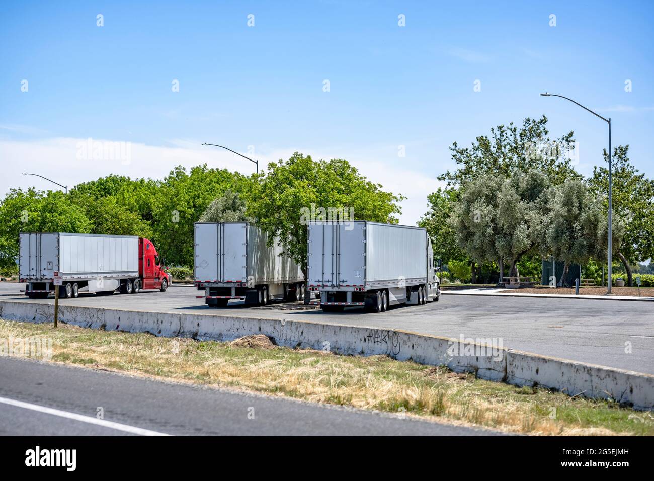 Group of big rigs semi trucks tractors transporting cargo in different semi trailers standing in a line by the side for a break on the rest area parki Stock Photo