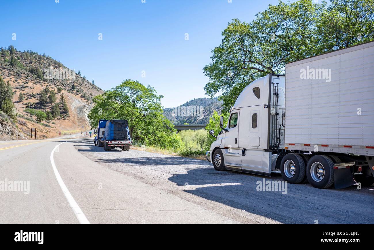 Group of big rigs semi trucks tractors with cargo in different semi trailers standing on the shoulder of the road take a break for truck driver rest i Stock Photo