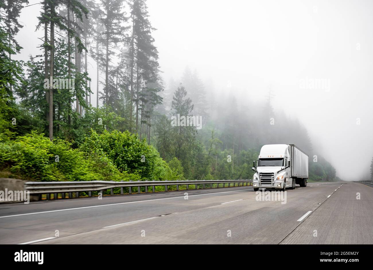 White big rig long haul semi truck transporting commercial cargo in dry van  semi trailer running on turning one way highway road with forest on the hi  Stock Photo - Alamy