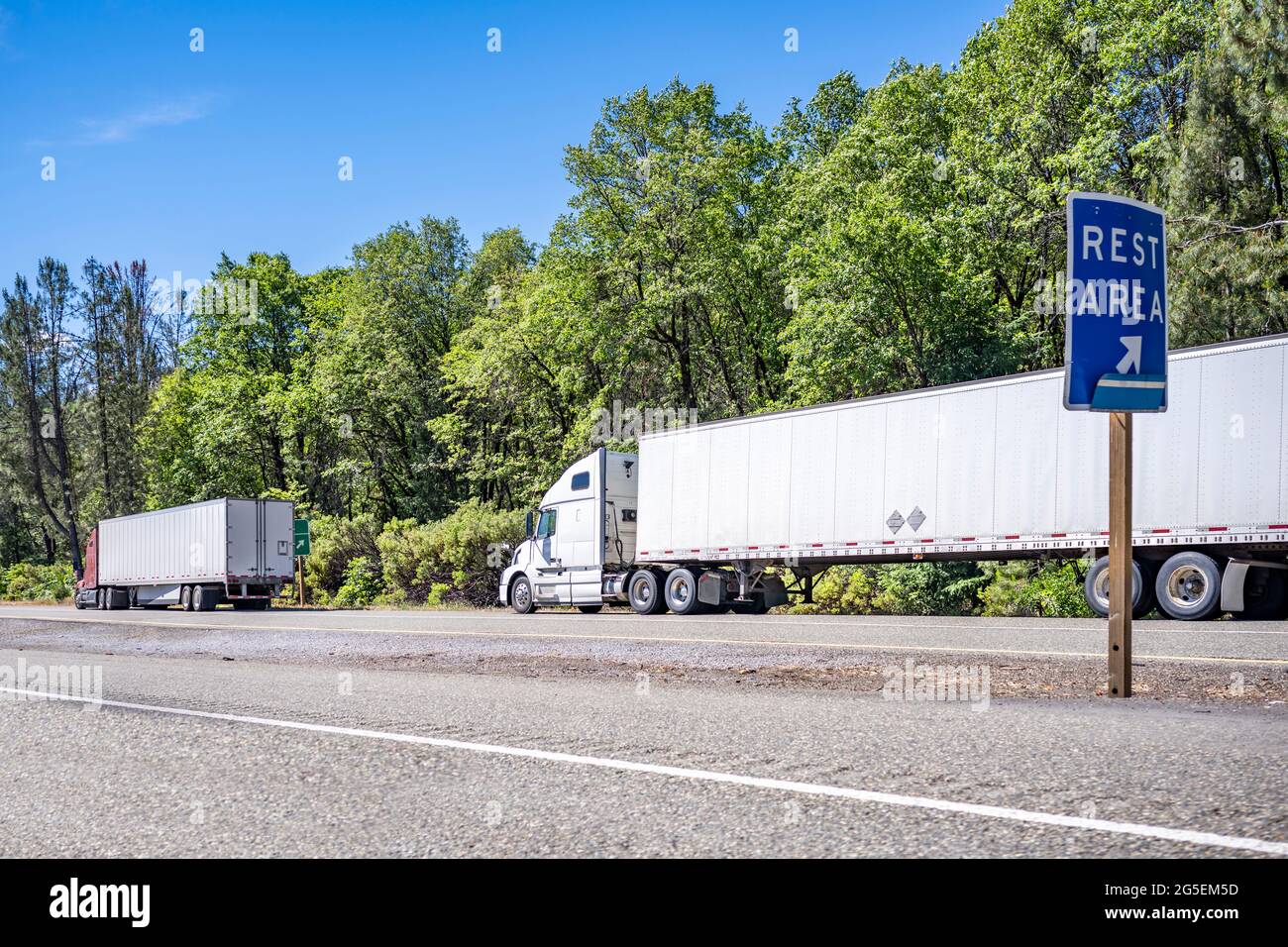 Group of big rigs semi trucks tractors transporting cargo in different semi trailers standing in a line by the side of the highway road for a break ou Stock Photo