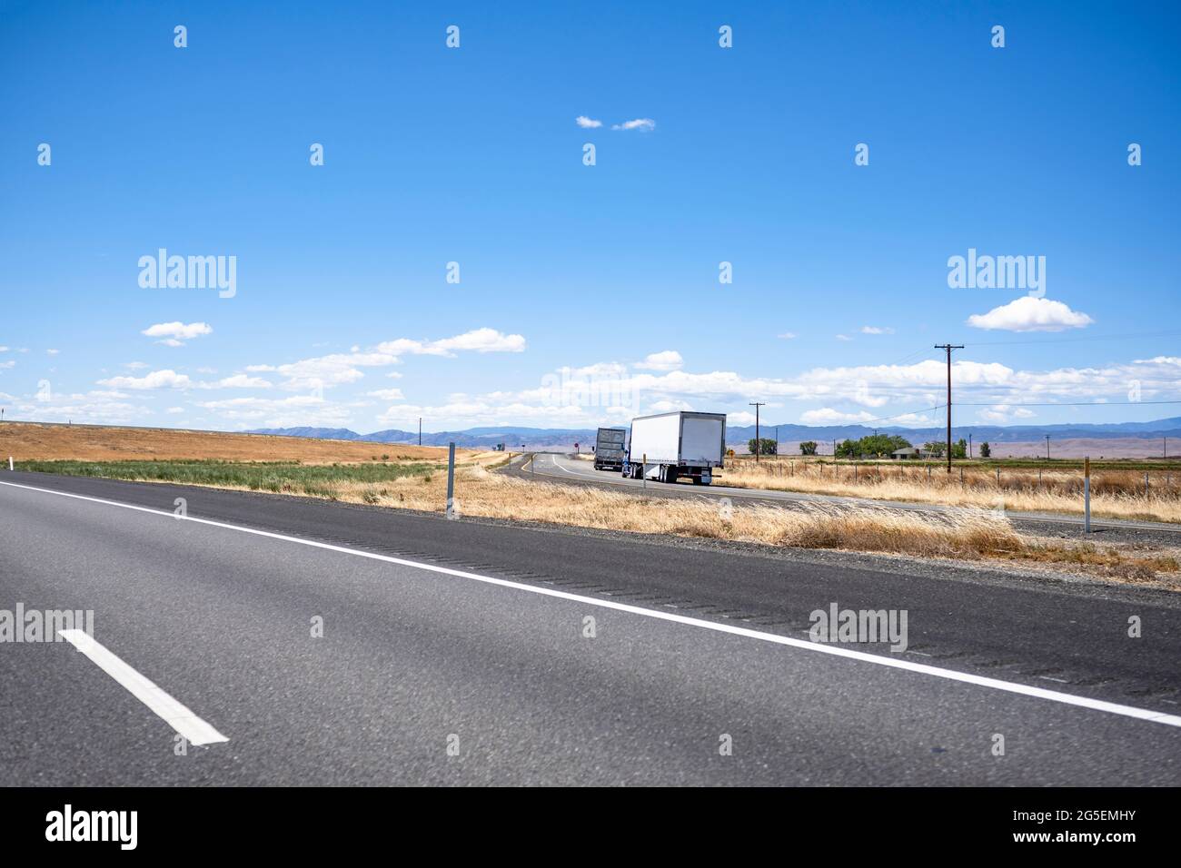 Group of big rigs semi trucks tractors caring cargo in different semi trailers standing on the shoulder of the highway exit intersection road take a b Stock Photo