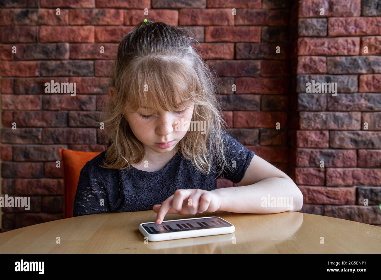 A little girl learns notes in a playful way, with the help of a piano on her phone. Stock Photo