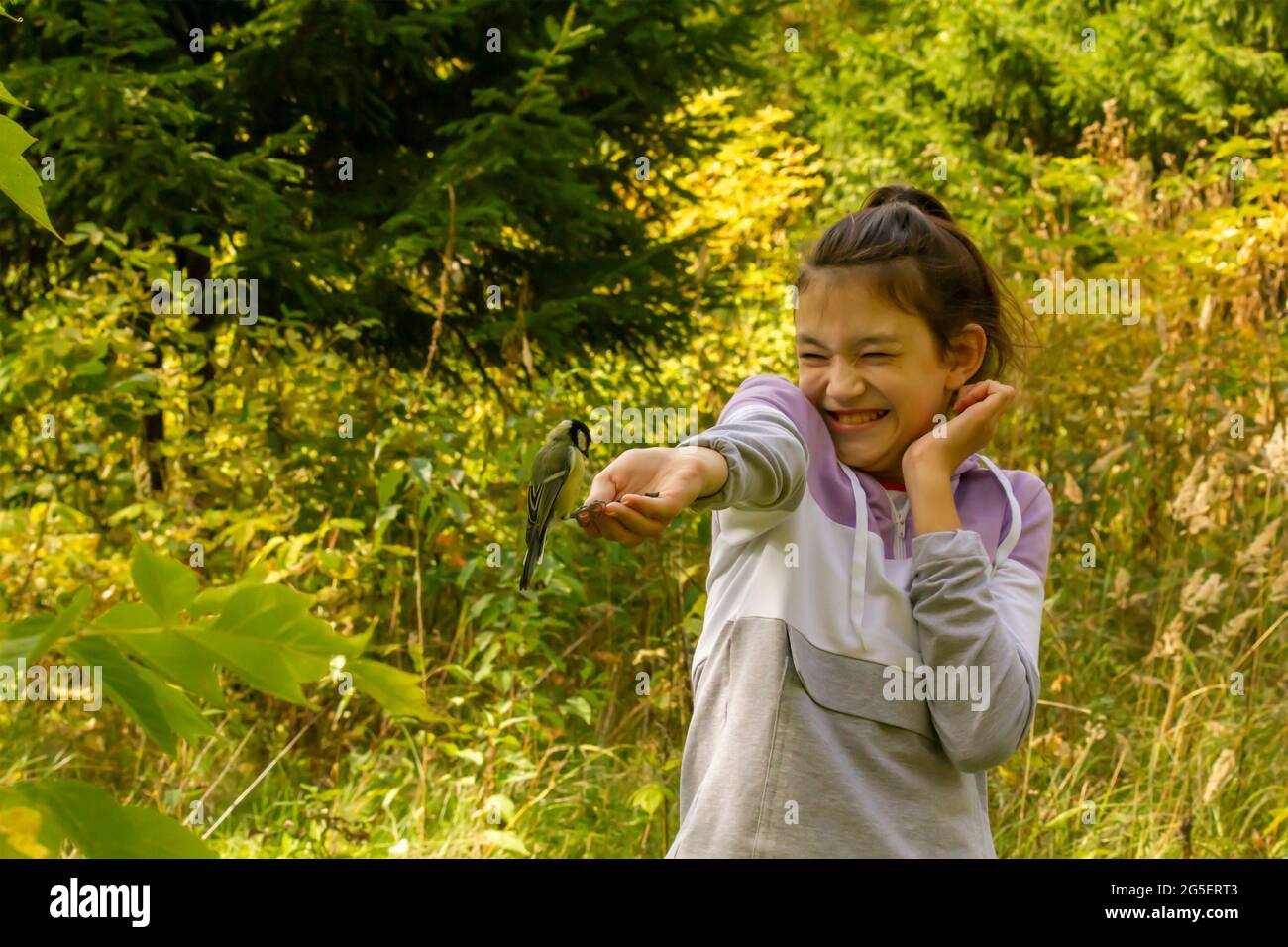 Laughing girl feeding birds in autumn forest. The concept of spending a joint family weekend in nature. Stock Photo