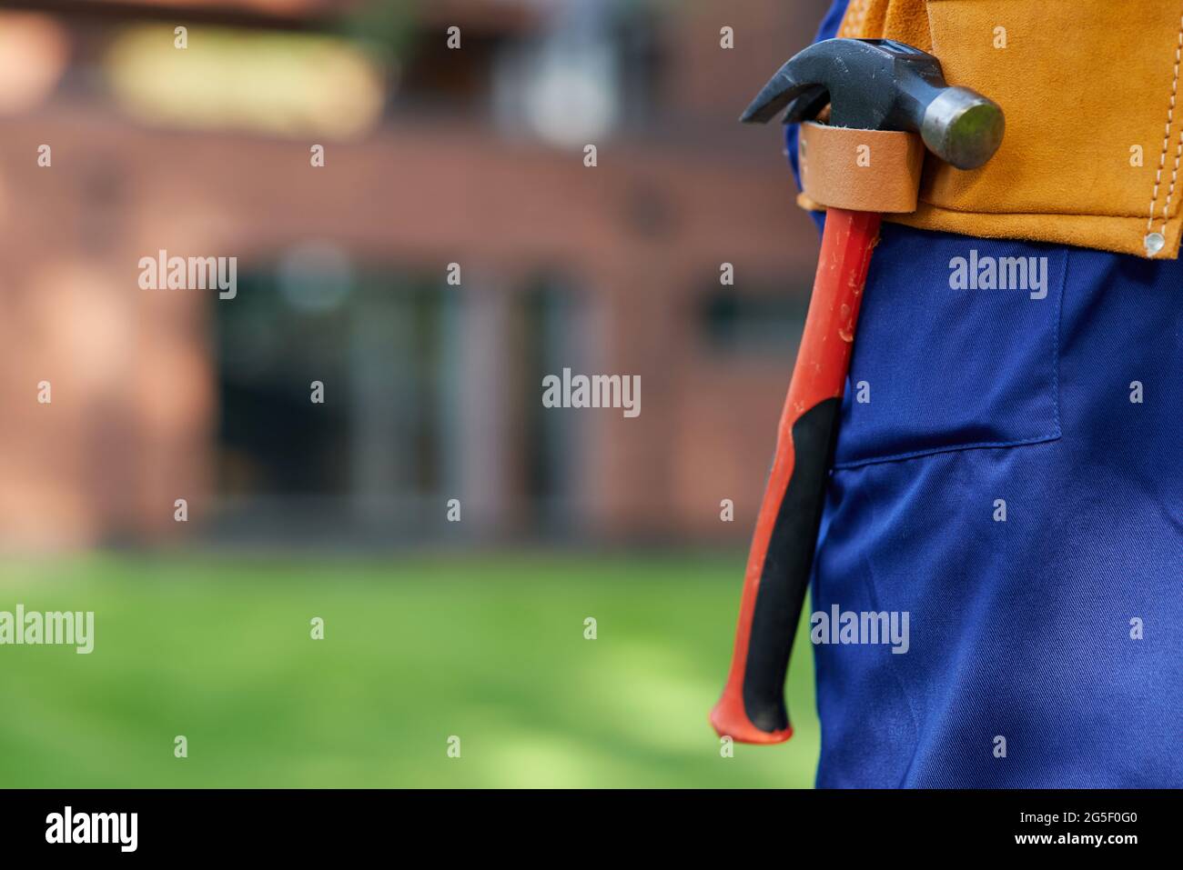 Close up of hammer hanging in tool belt on waist area of male builder in blue overalls Stock Photo