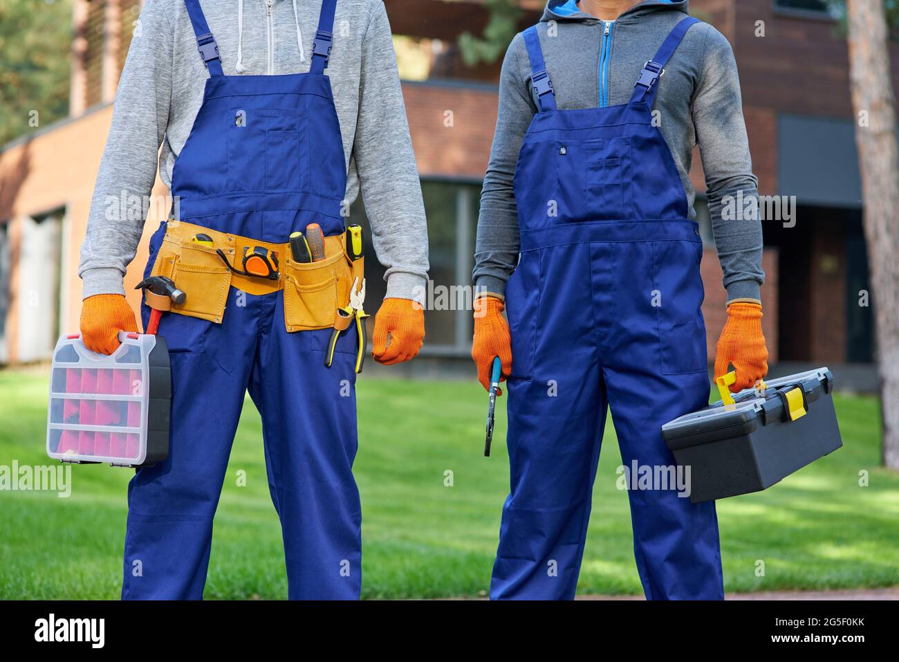 Cropped shot of two male builders in blue overalls carrying toolbox at construction site Stock Photo