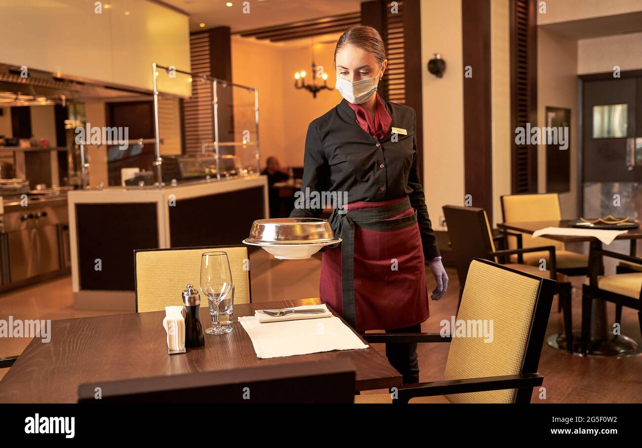 Female server bringing a dish under a steel lid Stock Photo