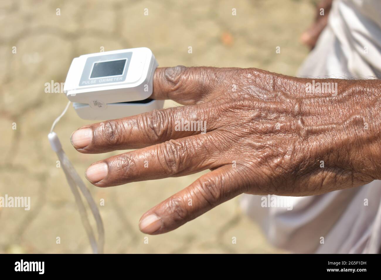 A closeup of a pulse oximeter attached to the index finger of an old ...
