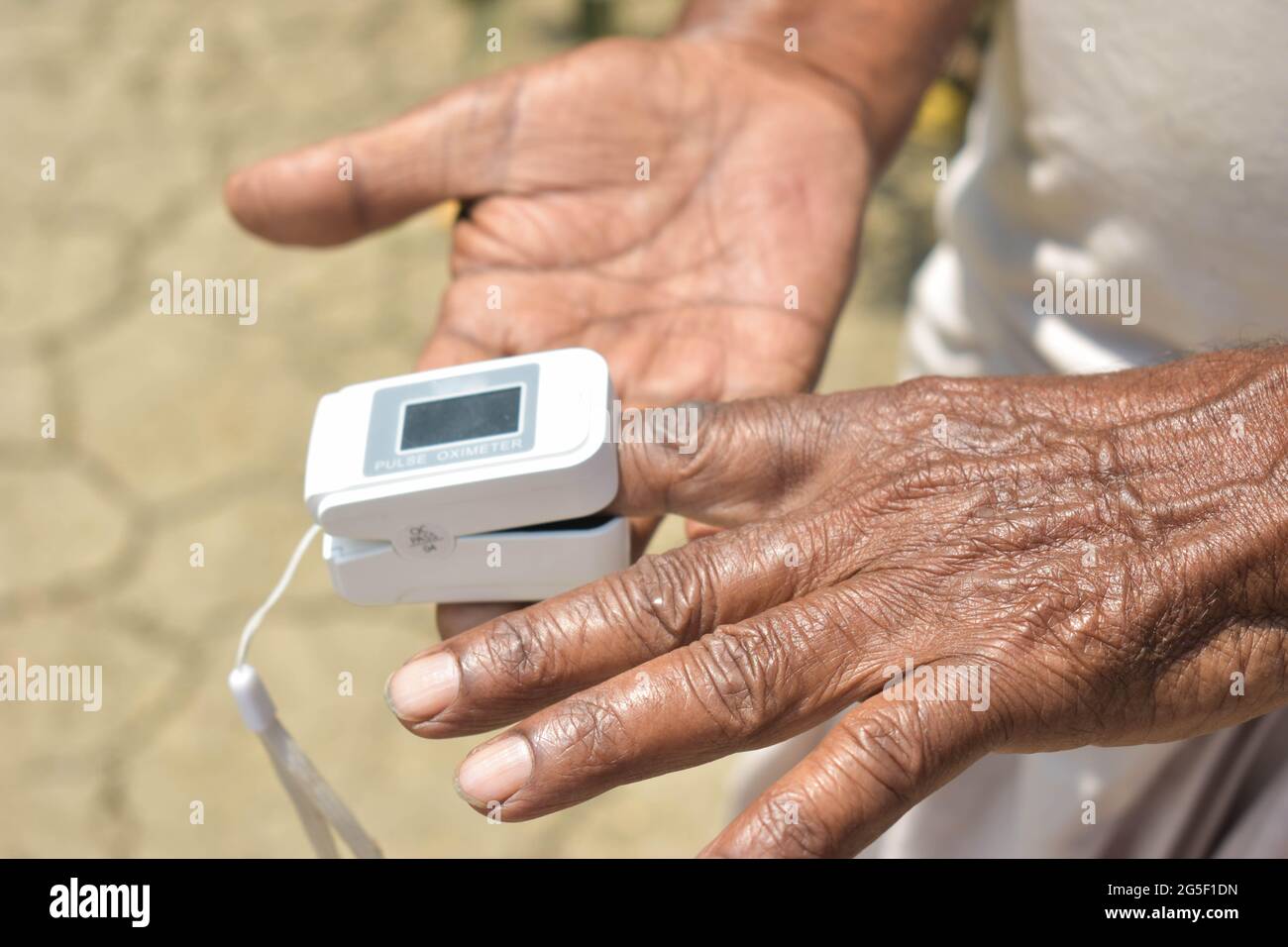 A closeup of a pulse oximeter attached to the index finger of an old ...