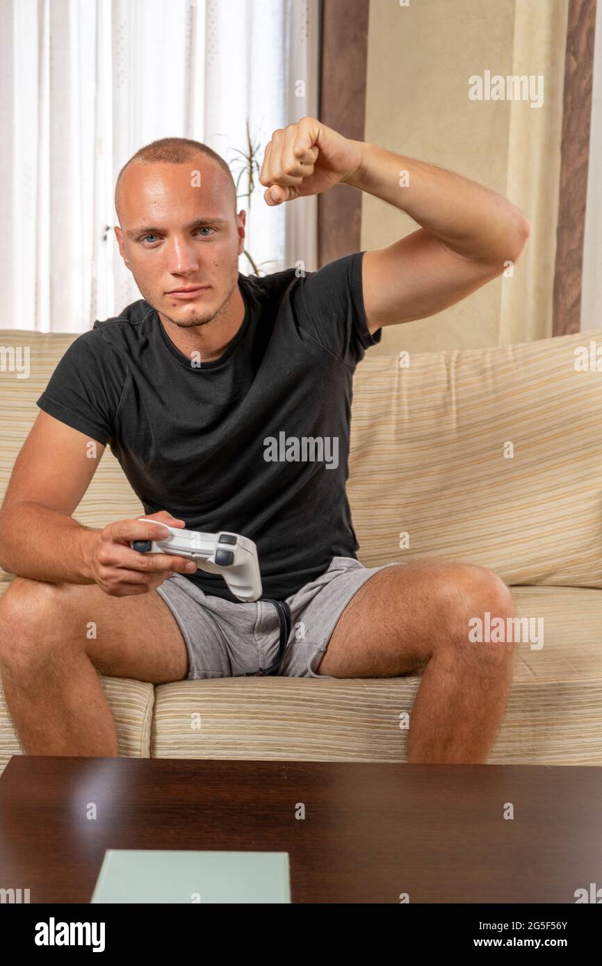 Attractive young man with blue eyes raising his fist in anger while playing game console in the living room at home. Gaming concept Stock Photo