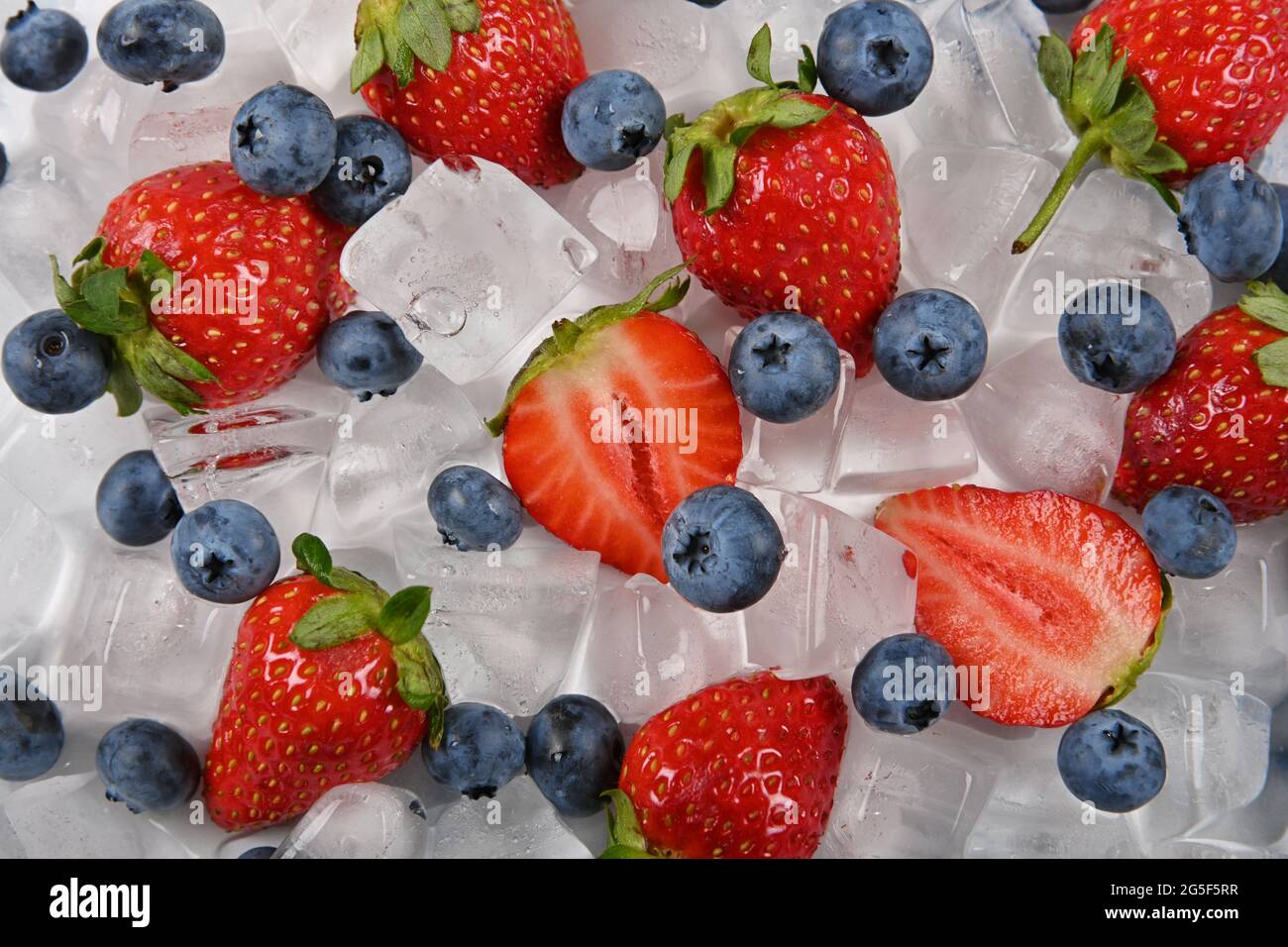Close up fresh red ripe strawberries, blueberries and ice cubes on table, elevated high angle view, directly above Stock Photo