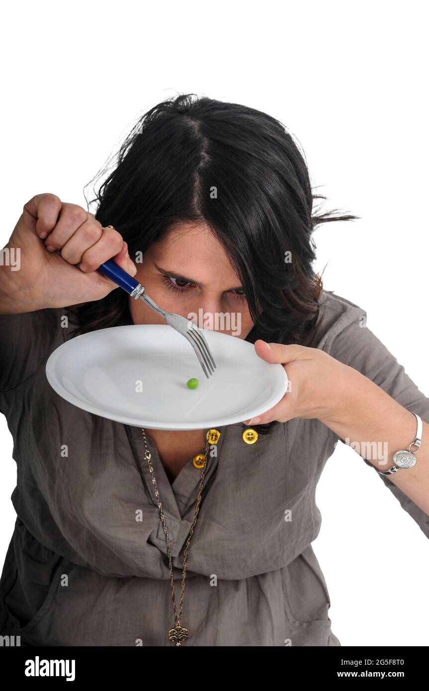 exaggerated approach to Eating Disorders. The sickness of the 21st century Anorexia and eating disorder concept young woman eats a single pea on a lar Stock Photo