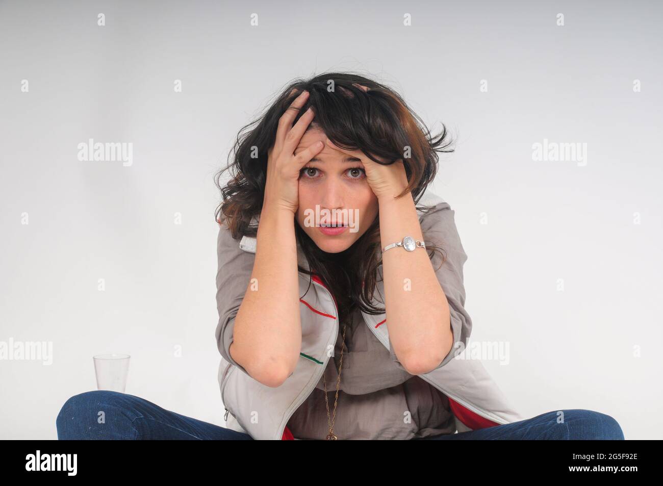 exaggerated and comic look at a young frightened woman hugging herself in fear studio shot on white background Stock Photo