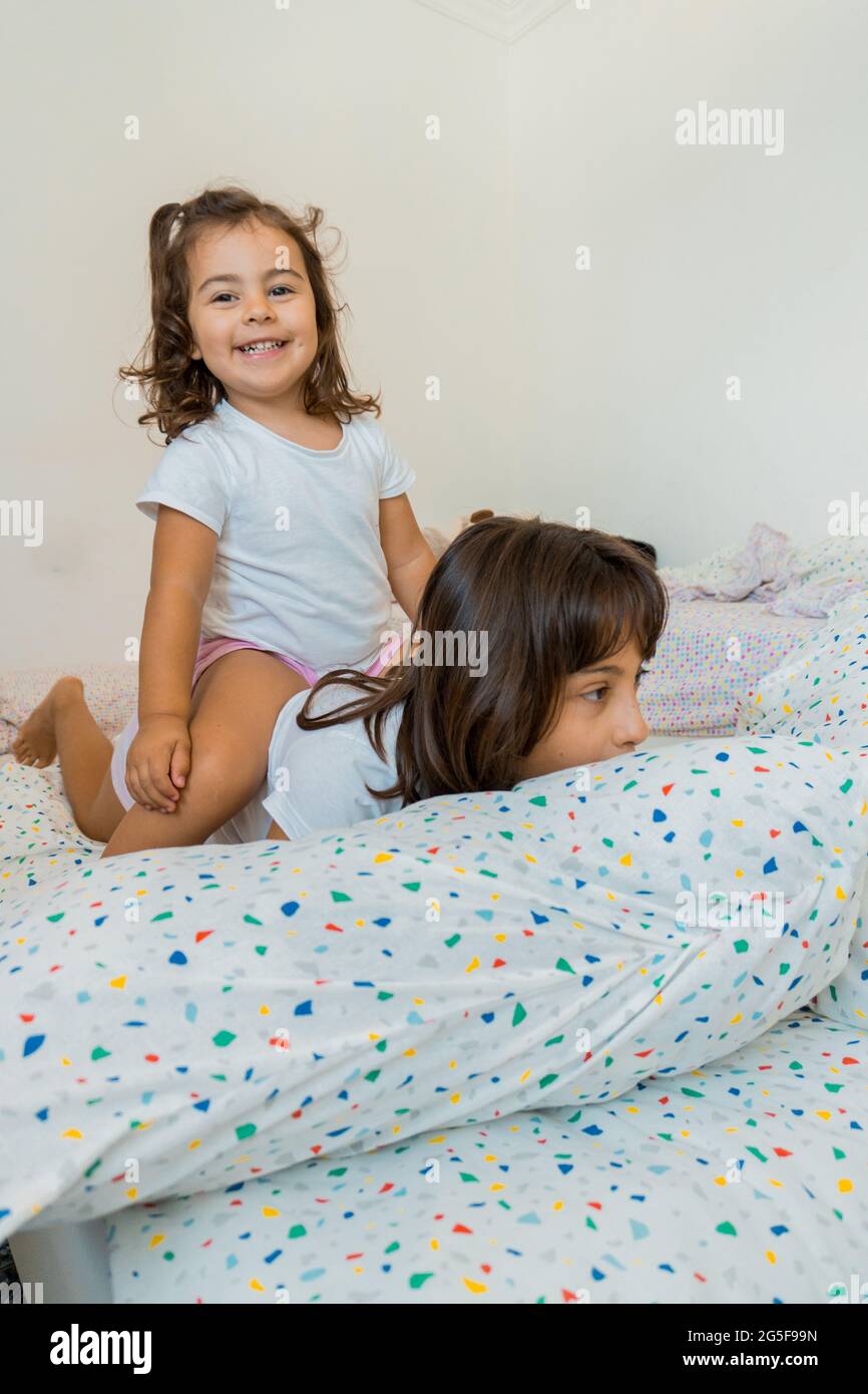 Two Caucasian girls, ages two and nine, are having fun together on their bedroom beds, playing and talking. Stock Photo