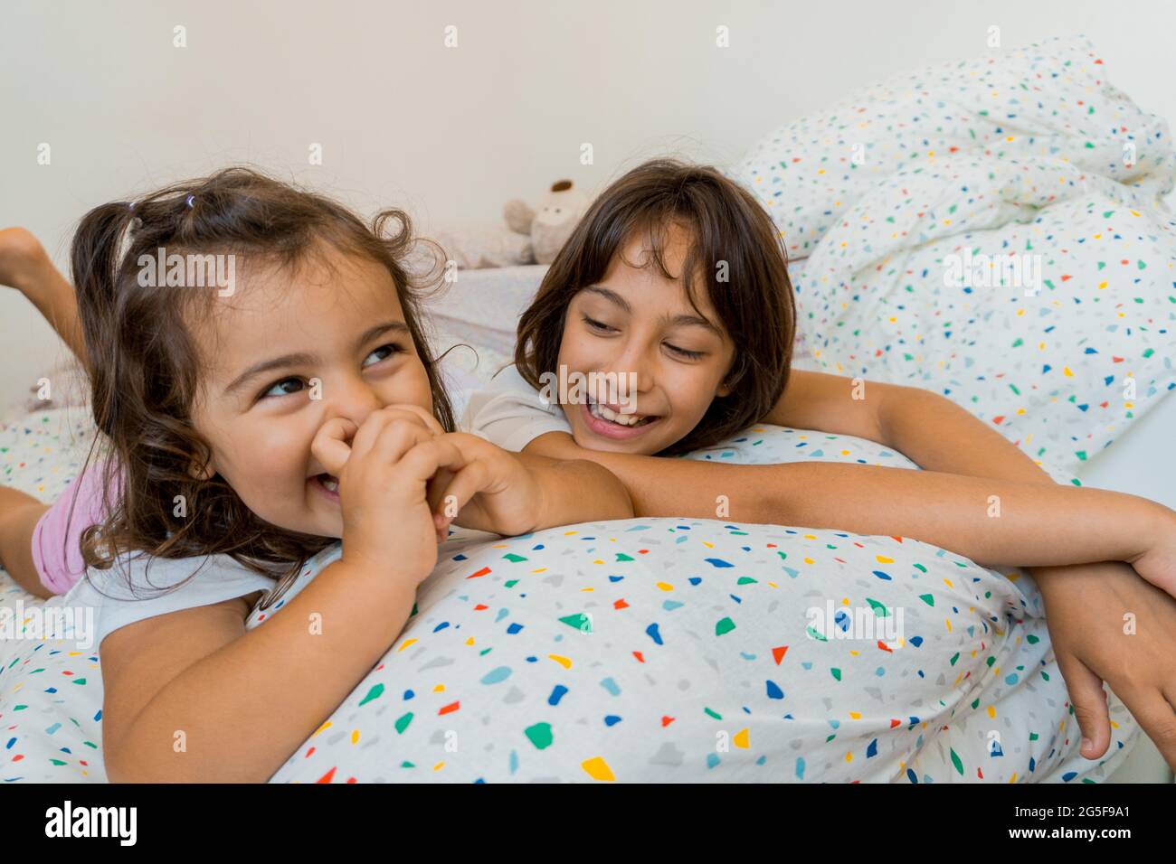 Two Caucasian girls, ages two and nine, are having fun together on their bedroom beds, playing and talking. Stock Photo