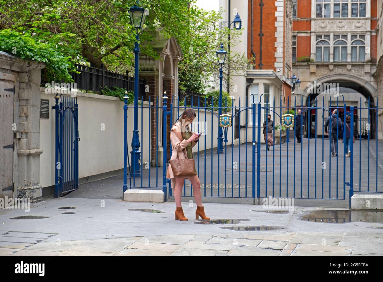 Young woman standing in street looking at mobile phone texting near Drapers Hall in the City of London UK  KATHY DEWITT Stock Photo
