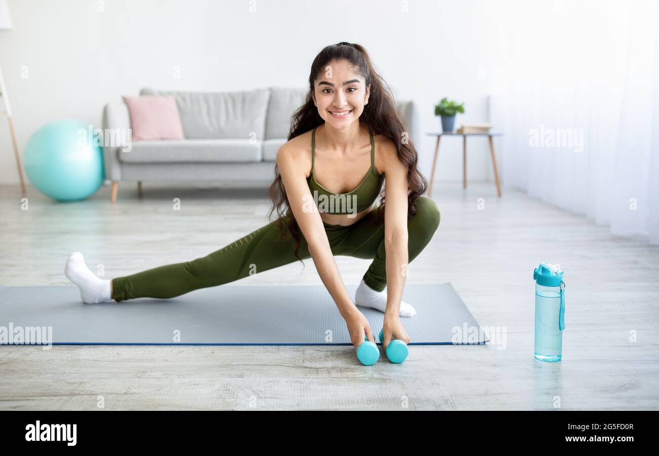 Young Indian woman doing stretching exercises with dumbbells on
