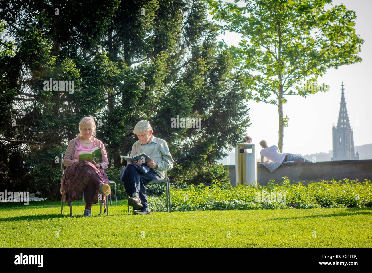An old couple reading books, enjoying the balm summer evening in the Rosengarten Park in Bern Stock Photo