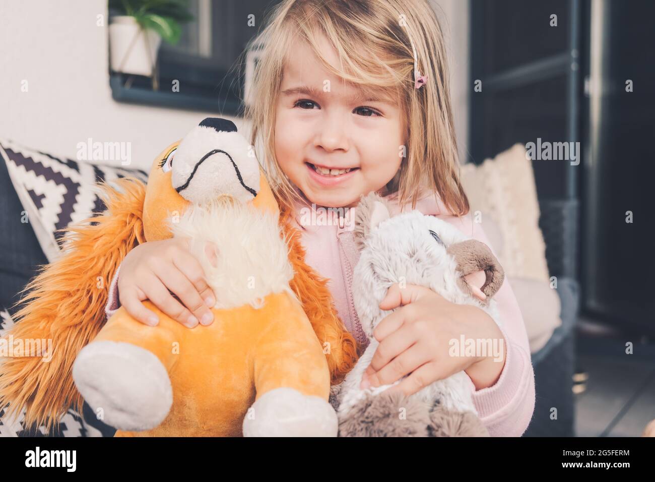 Little girl smiling and hugging two plush toys dog and cat Stock Photo