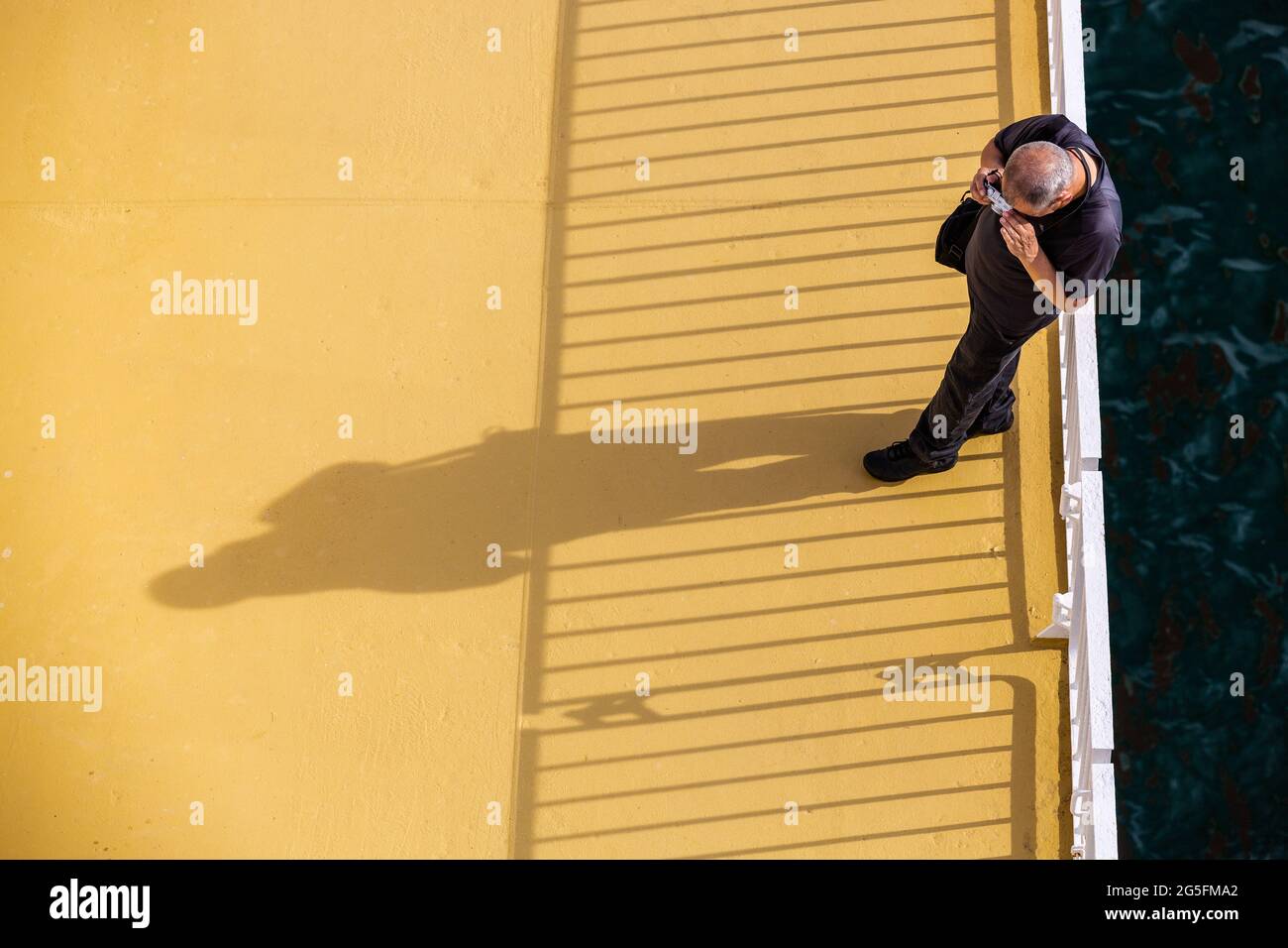 Photographer shooting his shadow leaning on the rail of a boat. Stock Photo