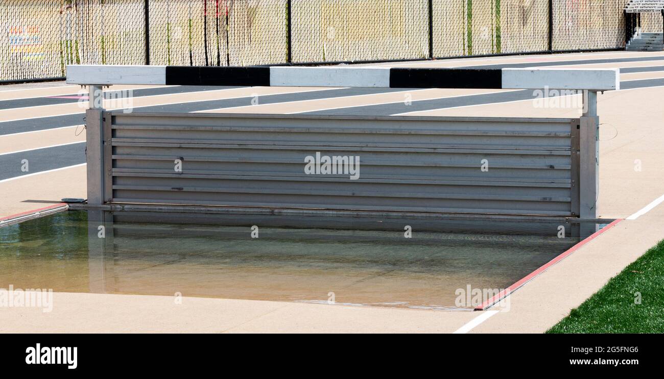 The water pit of a track and field steeplechase is full and set at the boys height for a race. Stock Photo