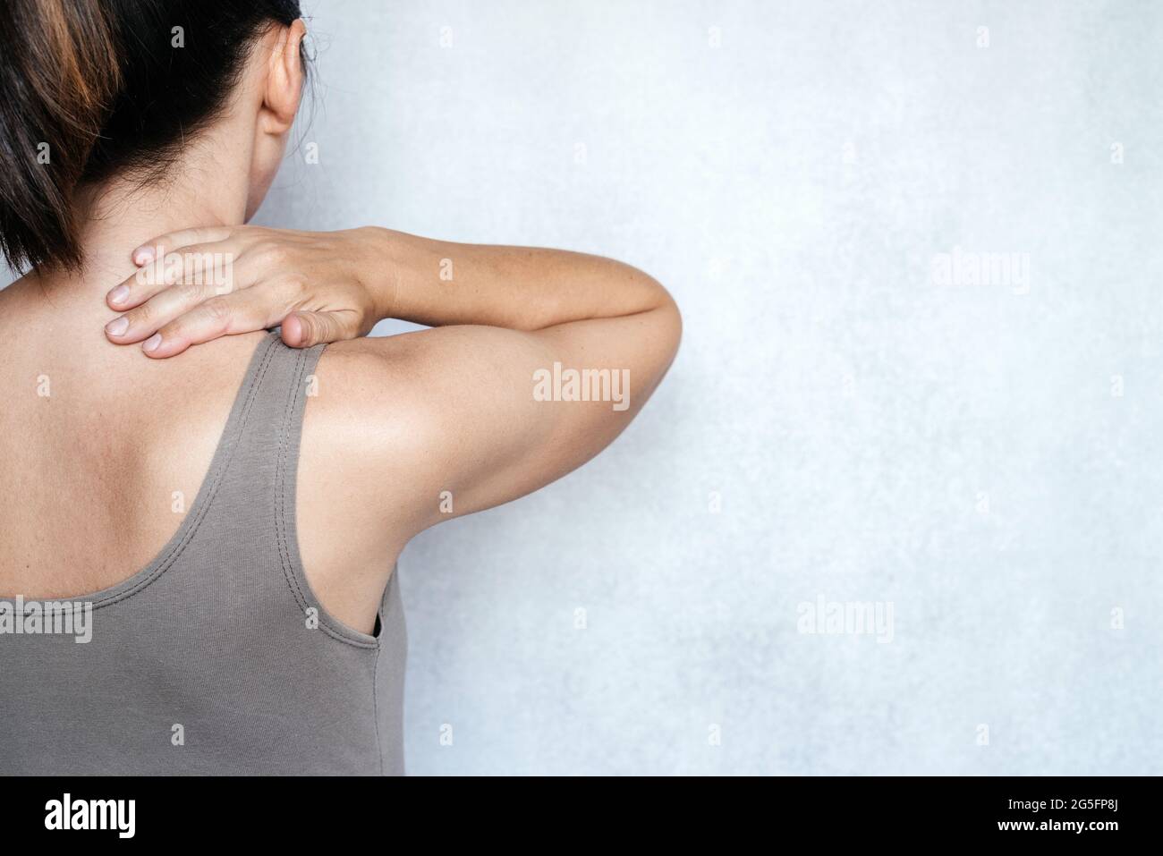 A woman suffering from neck pain and massaging her neck to releive pain ...