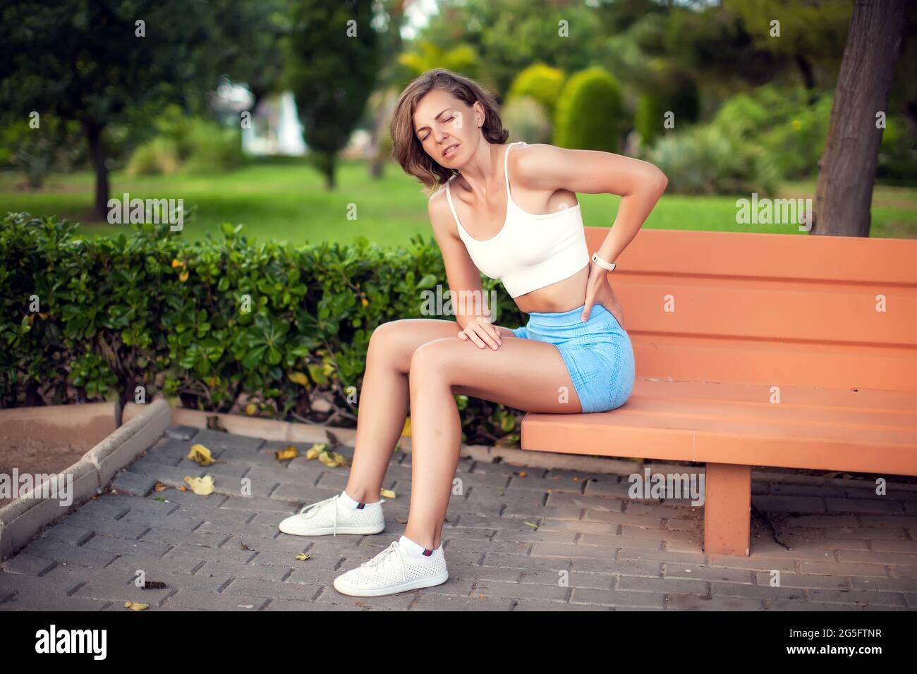 Back pain. Woman with back injury sitting on the bench outdoor. Healthcare, sport and lifestyle concept Stock Photo