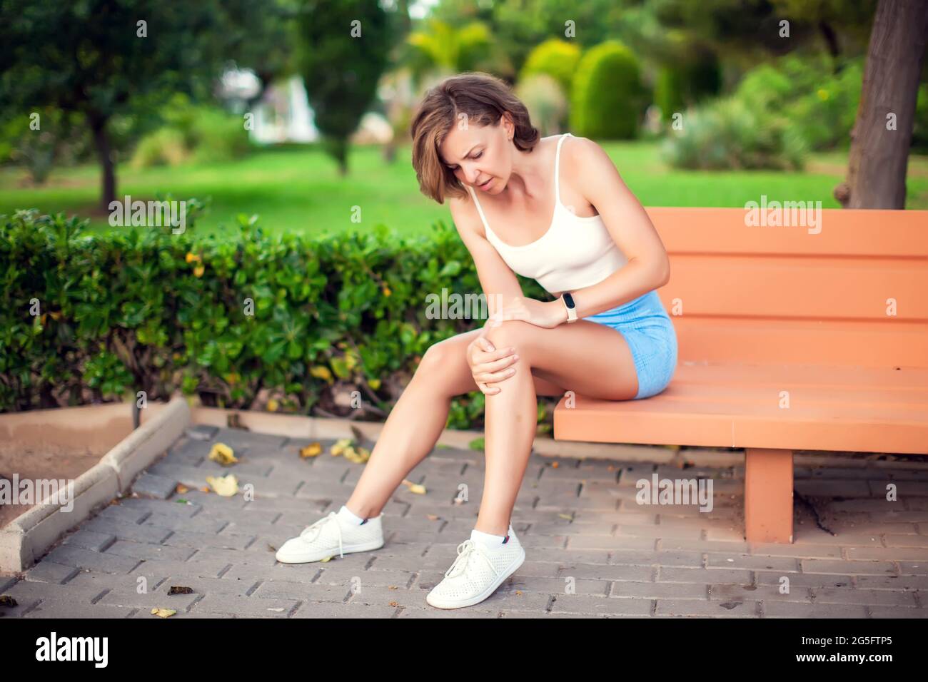 Knee pain. Woman with knee injury sitting on the bench outdoor