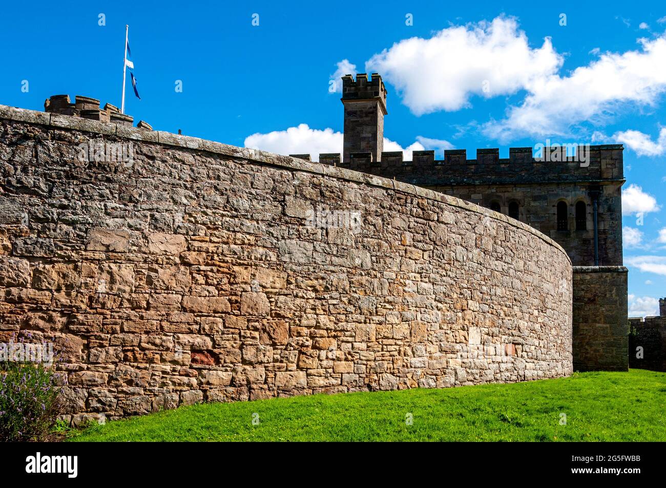 A 2-storey cell block of Jedburgh Prison in deep shadow is partly hidden by a high wall of dressed stone as the Saltire flies from a tower in sunshine Stock Photo