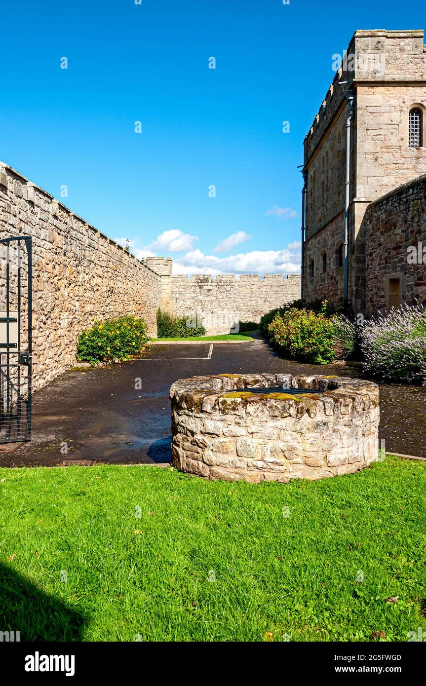 The prison well is situated in a mown lawn at the rear of a two-storey cell block in Jedburgh Castle Old Jail between a quadrant wall and outer wall Stock Photo