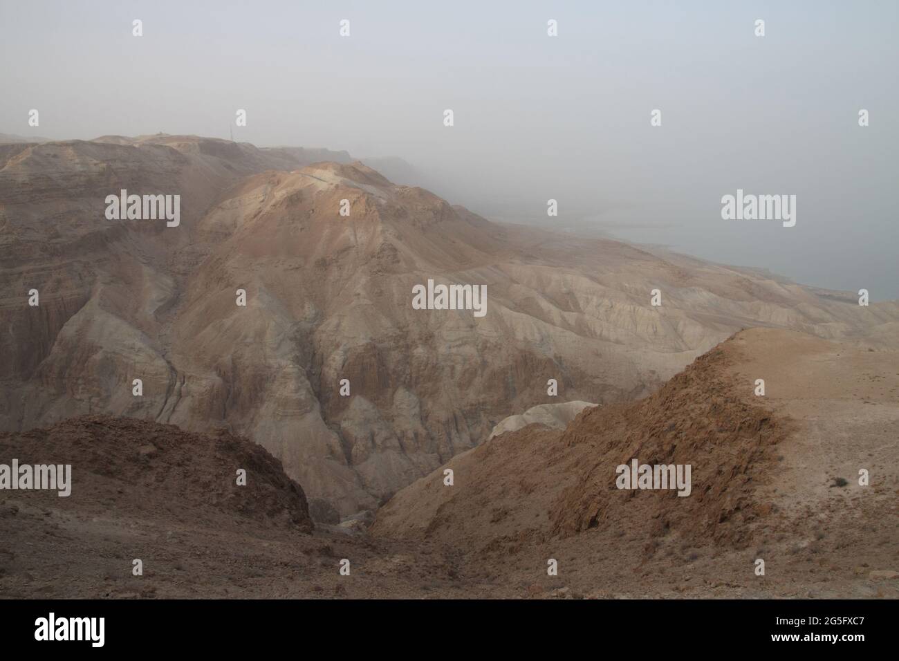 Awesome view at sunset of the steep walls of Nachal Dragot or Darga & it's ravine in the Judean Desert and the Dead Sea on an overcast and foggy day. Stock Photo