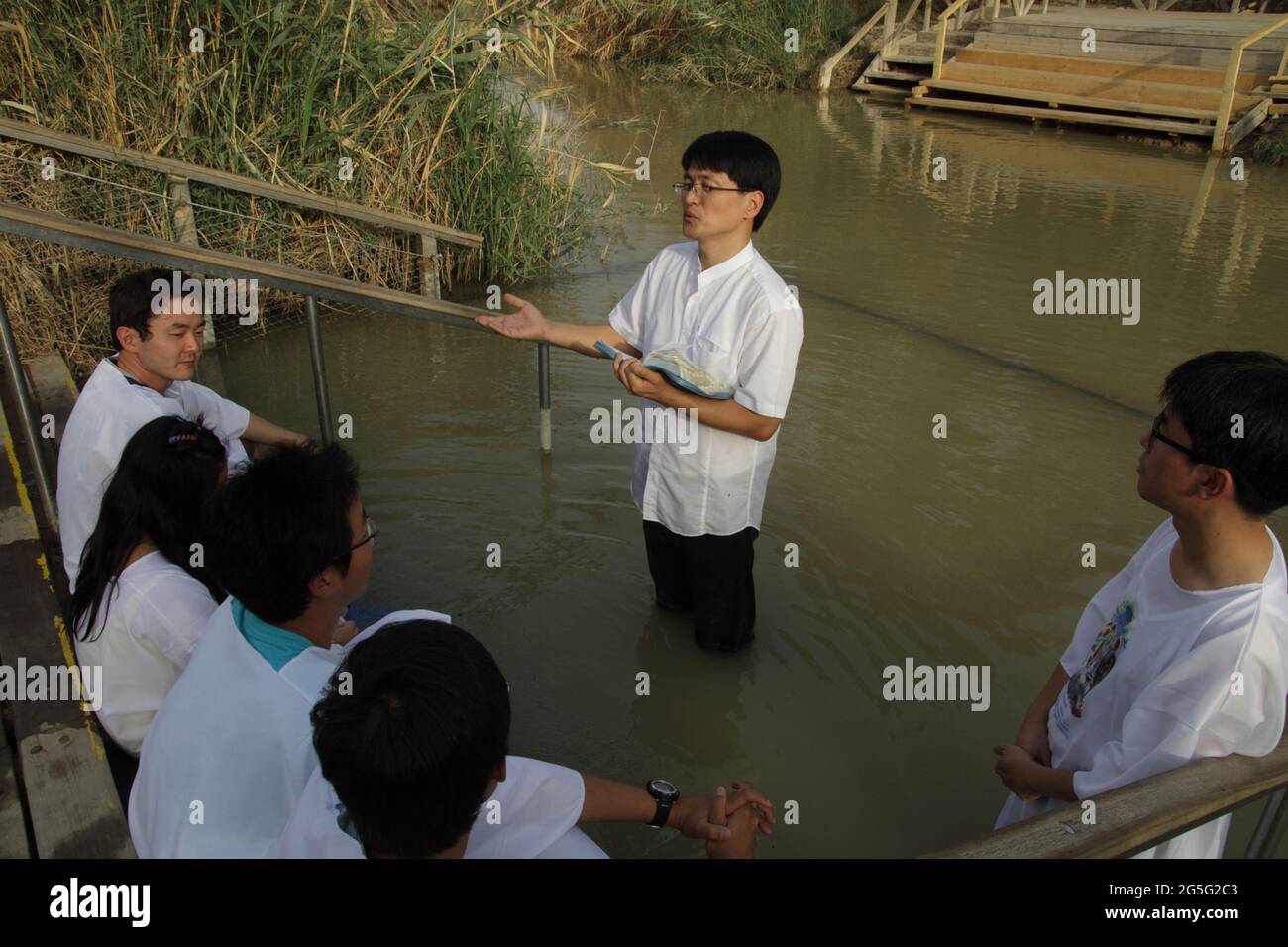 Korean Protestant youth wear white gowns listen to the pastor read the Bible before baptising in the Jordan River in Qasr El Yahud where Christ did. Stock Photo