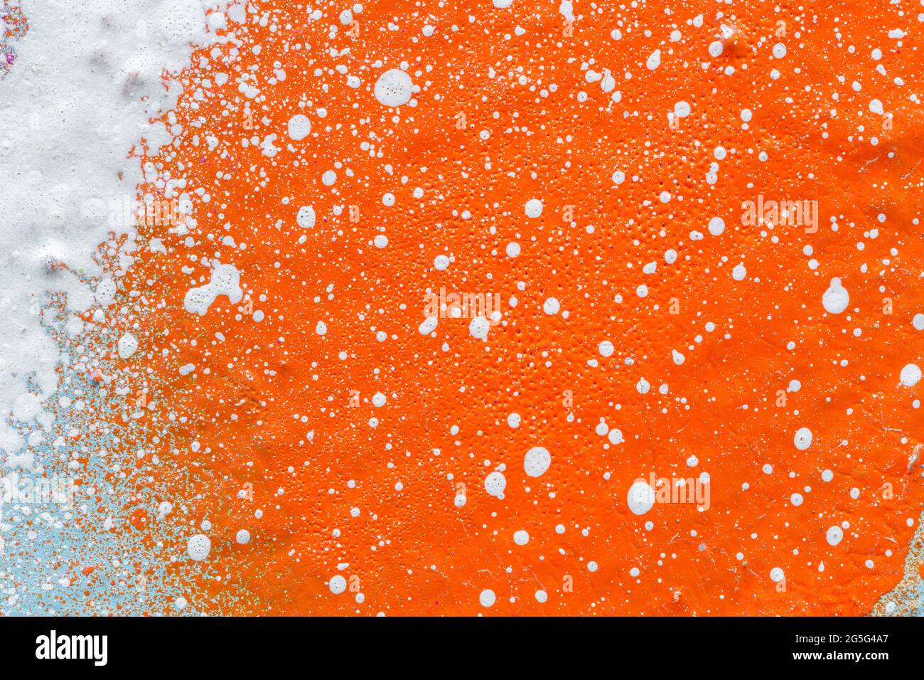 Macro close-up of a orange spray paint with white splashes. Abstract full frame textured splattered graffiti background with copy space. Stock Photo