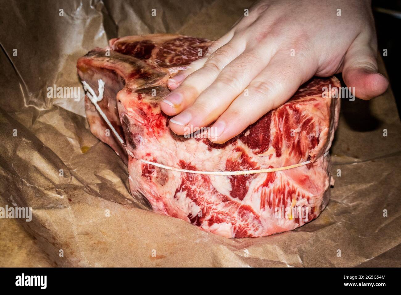 Raw two bone standing rib beef roast with hand rubbing olive oil into it on butchers paper Stock Photo