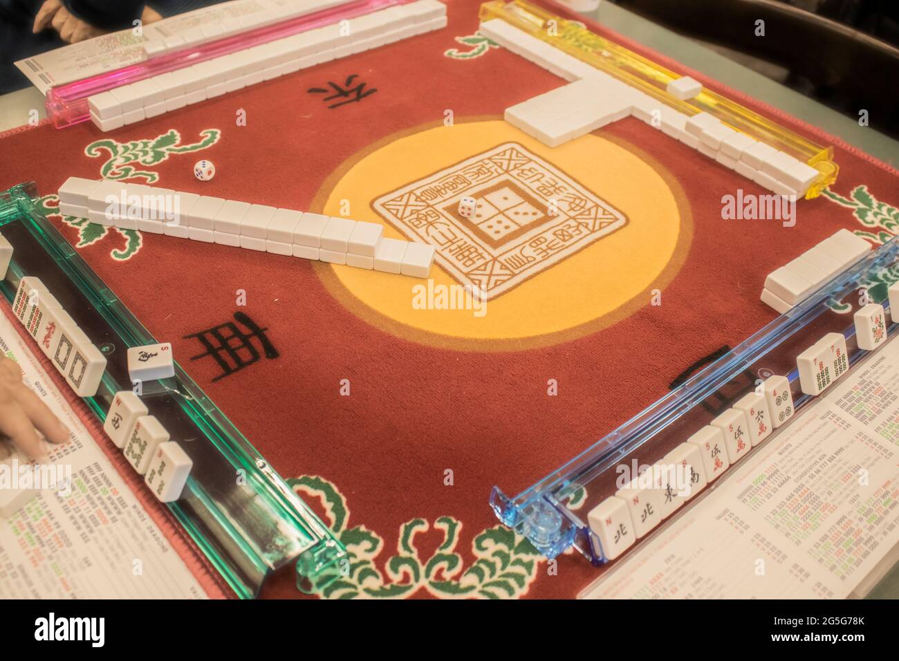 Table where Mahjong - the Mandarin tile-based game - is being played on a colorful mahjong mat with a dice in the middle - selective focus Stock Photo