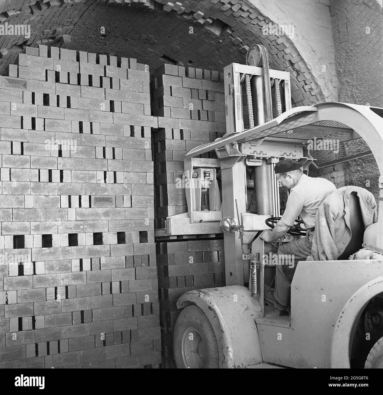 1950s, historical, male worker operating an electric forklift to move a large stack of bricks, Bedford, England, UK. The outbreak of WW1 led to developments of machines with rising and lowering platforms and first forklift is considered to be a vehicle called a Tructractor made in 1917. Developments in the 1940s saw forklifts introduced with a rechargeable battery so they could be used all day long. Stock Photo