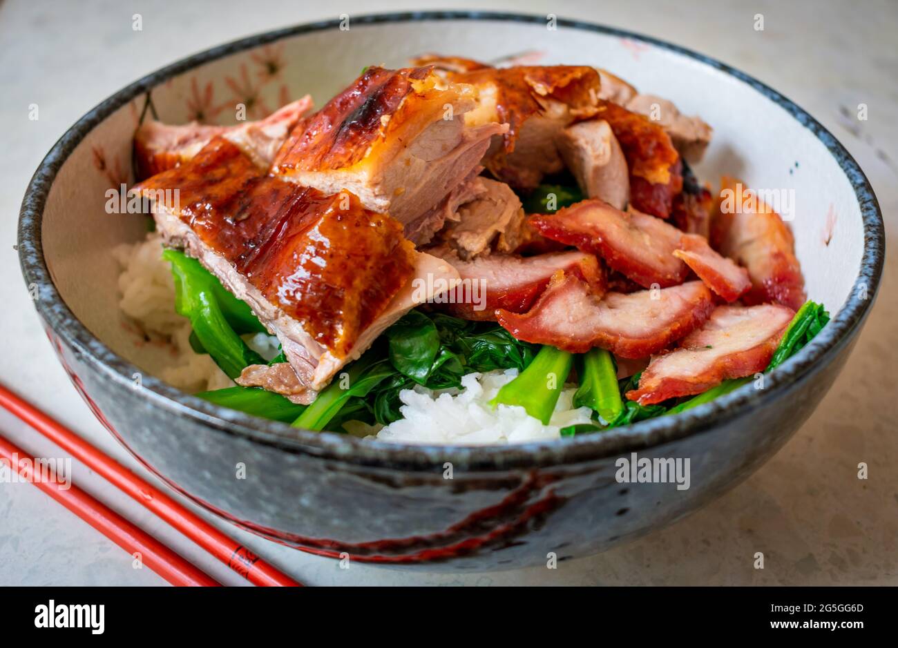 Cantonese roast duck with honey roast pork and green vegetables in a bow with rice. Stock Photo