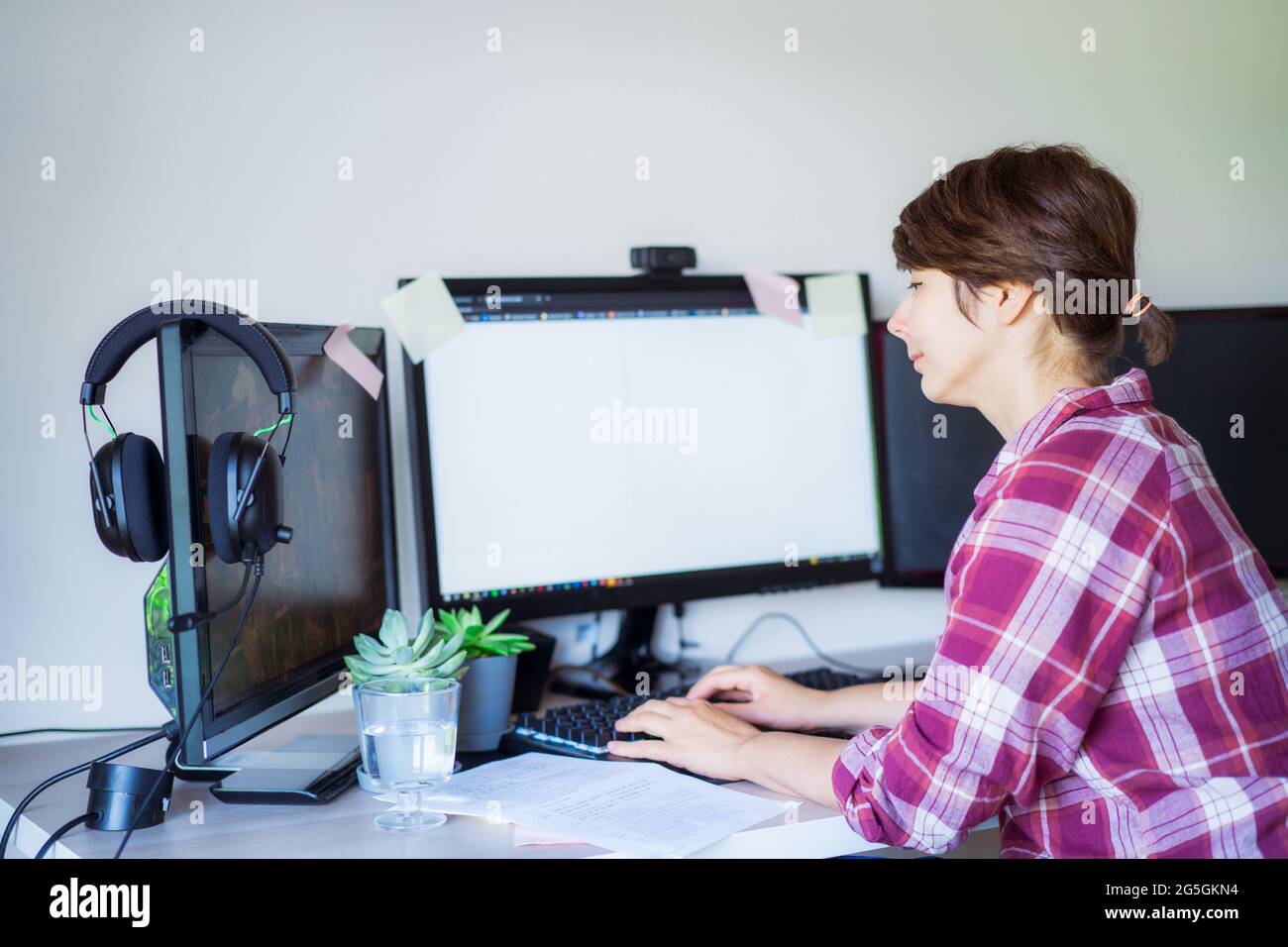 Side view woman working on pc with few monitors at home working space. Remote work concept. Freelancer workspace. Selective focus. Copy space. Stock Photo