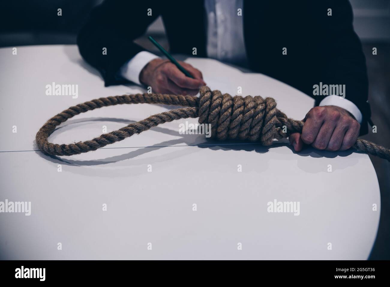 Young man preparing to commit suicide by hanging. He writes a farewell letter. Stock Photo