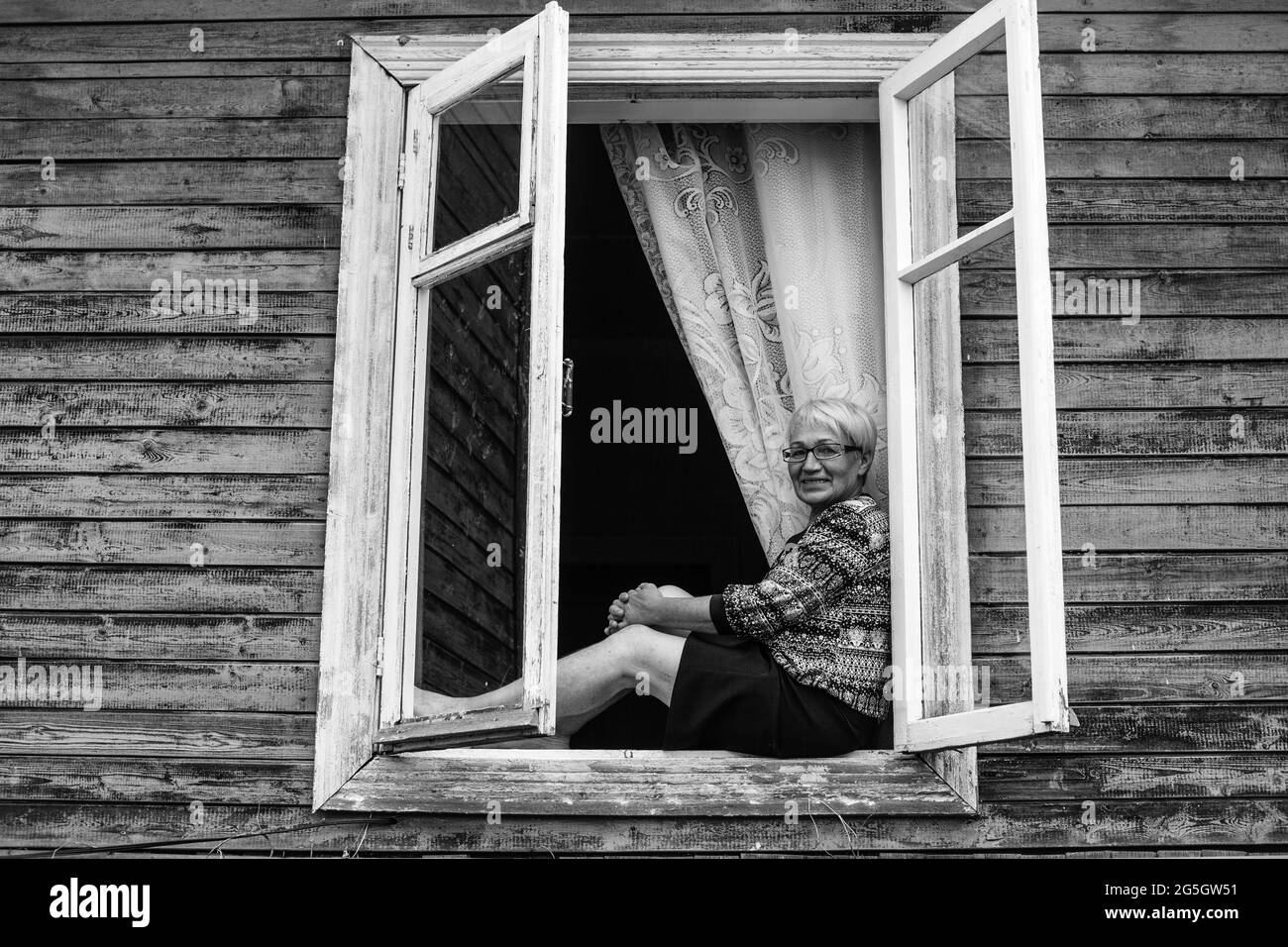 An adult woman sitting on the window of a village house. Black and ...