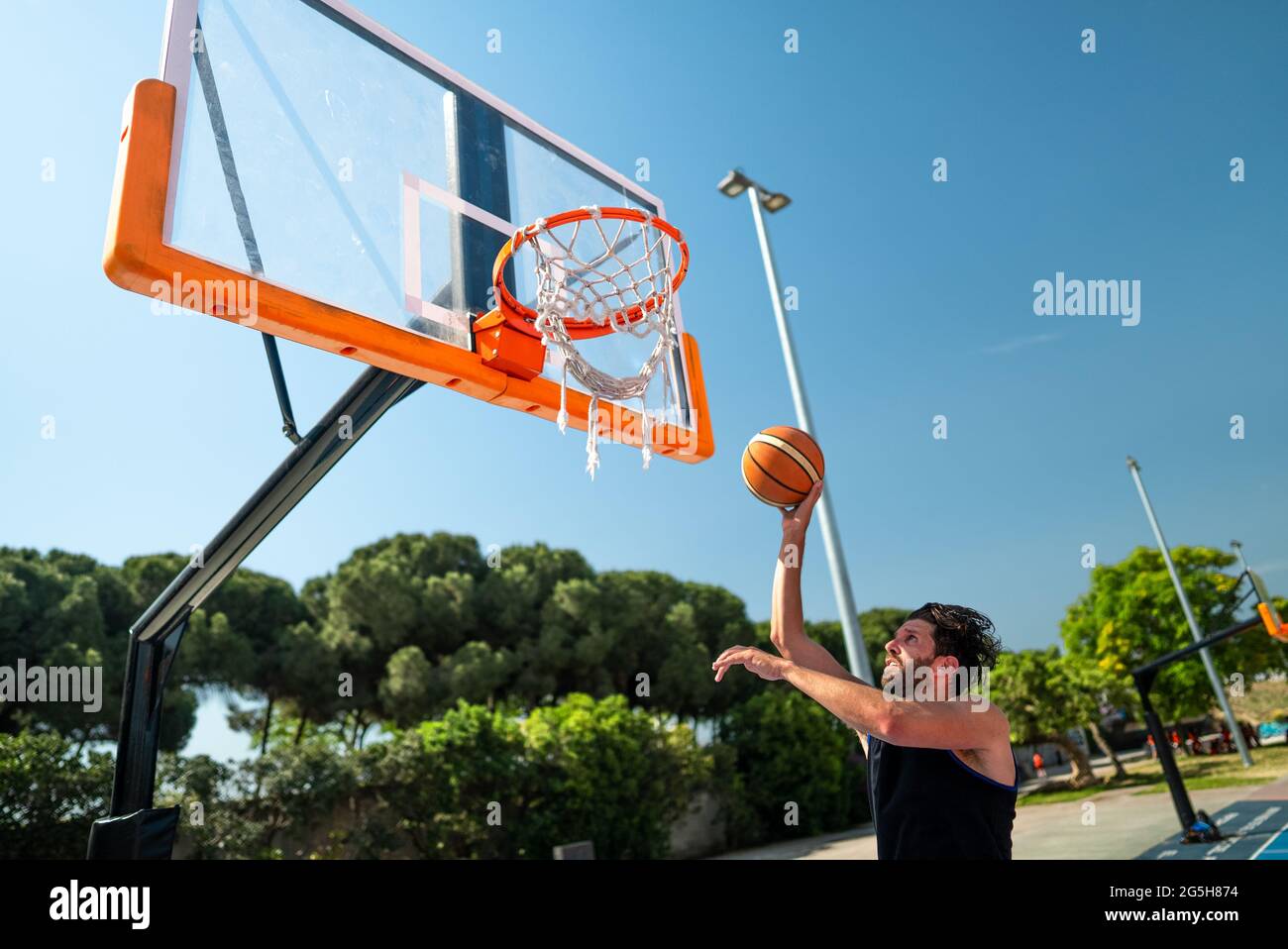 Male sportsman playing basketball throwing the ball at playground, doing successfully slam dunk view from behind. Precision shot Stock Photo