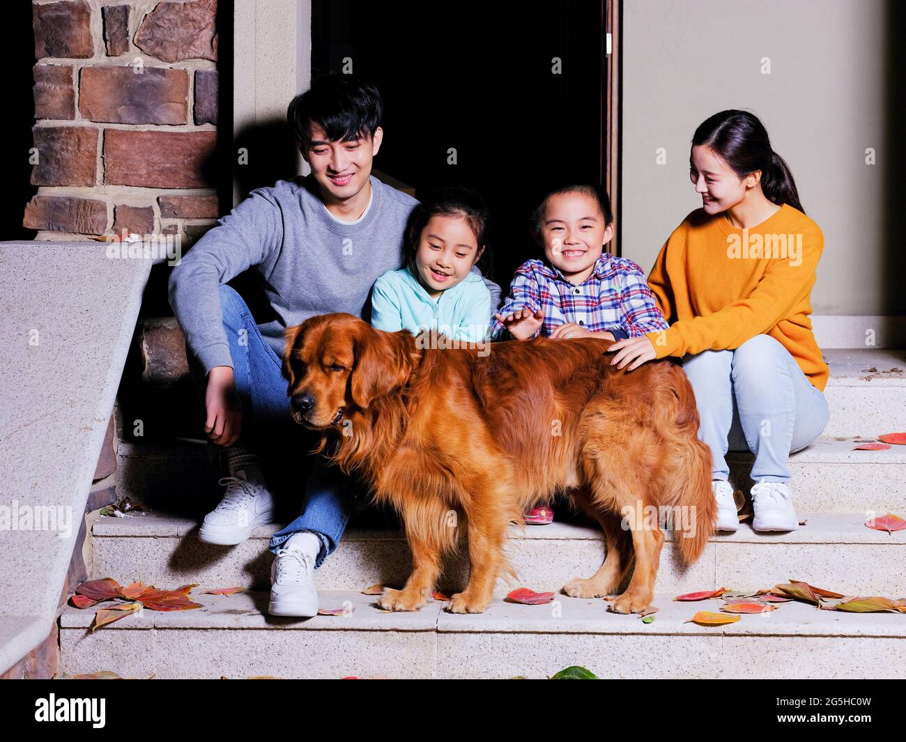 A happy family of four sitting on the steps with their pet dog high quality photo Stock Photo
