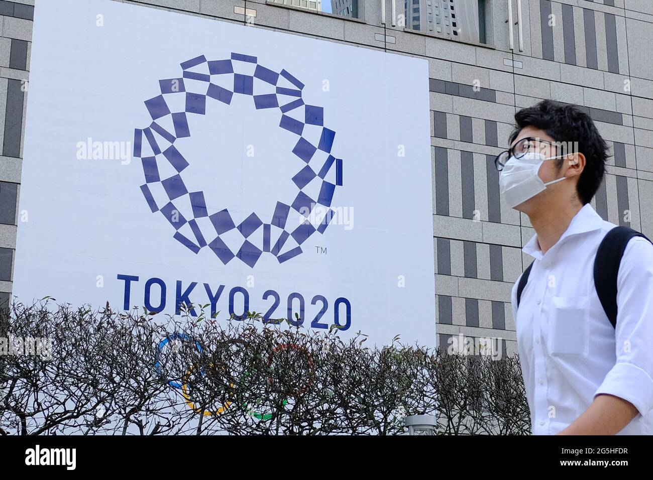 Tokyo, Japan. 25th June, 2021. A man wearing a face mask as a preventive measure against the spread of coronavirus walks past a banner for the upcoming Tokyo 2020 Olympics in front of the Tokyo Metro Government building. Credit: James Matsumoto/SOPA Images/ZUMA Wire/Alamy Live News Stock Photo