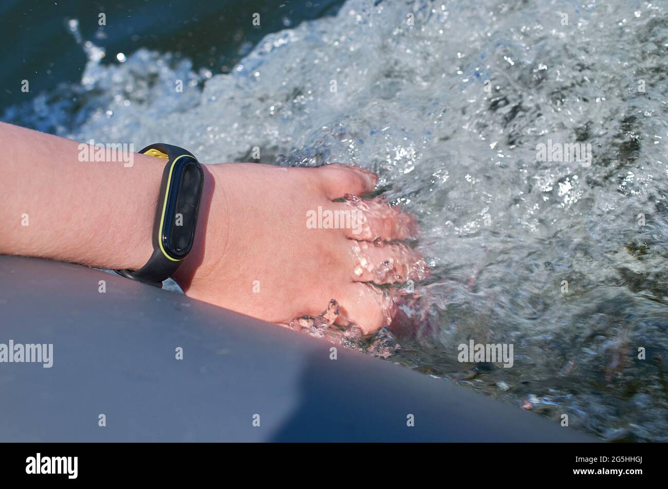 A teenager's hand with a waterproof fitness bracelet is lowered into the water. Stock Photo
